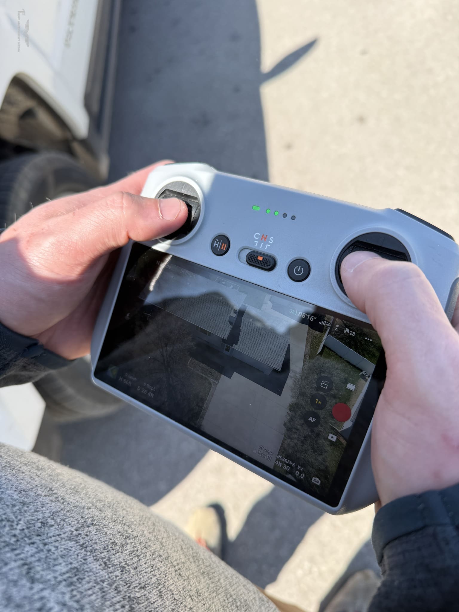 Part 107 Certified Drone Pilot operating a drone controller with live aerial view of a residential property on the screen, capturing real estate photos in Spearfish, SD for Odrix Media's Drone Photography Services.