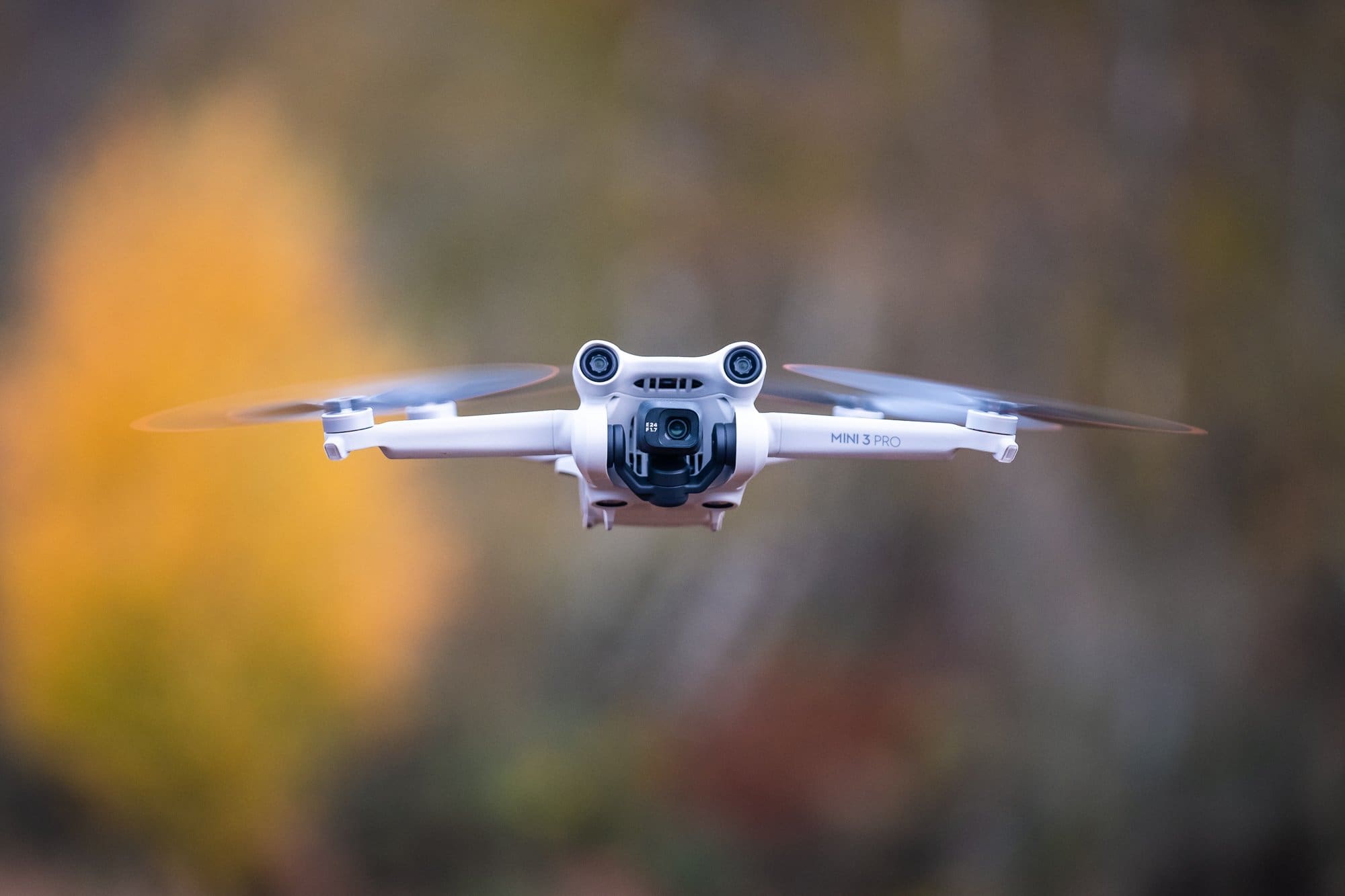 Close-up of a DJI Mini 3 Pro drone in flight, with blurred autumn foliage in the background. This advanced drone is used by Odrix Media for professional drone photography and videography services in Spearfish, SD.