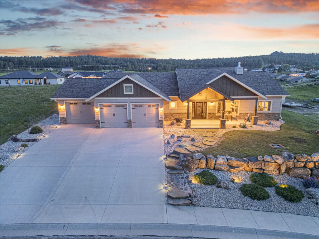 Drone photo of a modern single-story home in Custer, SD at sunset, captured by Odrix Media to highlight professional real estate photography services including architectural detail, exterior lighting, and landscape design.